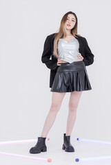 Fashion asian pretty young woman model pose playfully confident wearing silver corset top black pleated leather skirt black jacket expressing trendy streetwear style creative against white background.