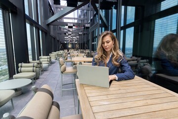 In a modern office, a focused woman works on her sleek laptop, surrounded by stylish decor and city skyline views that boost her creativity and productivity, creating an inspiring experience