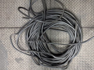 A coiled bundle of dark electrical cables rests on a textured, grey metallic diamond plate floor.