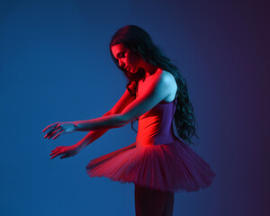 Dramatic 3/4 portrait of ballerina in red tutu and pointe shoes under moody blue and red neon...