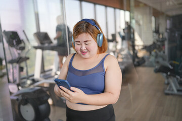Female with smart phone after workout at Gym. Obese asian woman watching online workout training class.