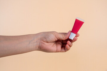 Red lipstick, small tube, and empty space and hand on cream background.