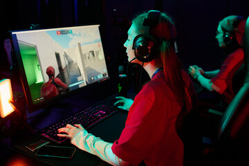 Caucasian teenage girl wearing headset playing computer game on gaming monitor in esports team...