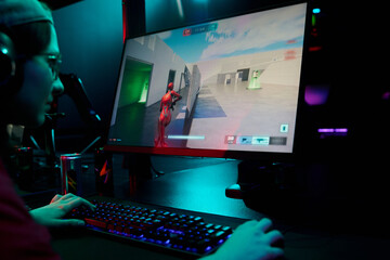 Teenage Caucasian girl gamer wearing headset playing first shooter video game on computer monitor in esports gaming setup, hands on keyboard and mouse, focused on screen © pressmaster