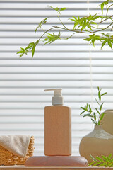 Amber pump bottle with green leaves and white towel set on a wooden bath counter. Clean, naturally...