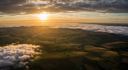 Aerial view of lush green fields under a dramatic sunset sky with clouds rolling over hills