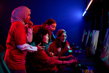Diverse group of teenage girls gaming together at esports event, including Asian, Caucasian, and Middle Eastern teenagers using computers, showing excitement and teamwork