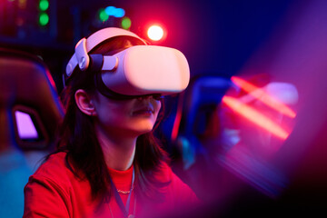 Teenage Caucasian girl wearing virtual reality headset sitting in gaming chair participating in...