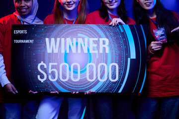 Diverse group of teenage girls standing together holding large esports tournament winner check for...