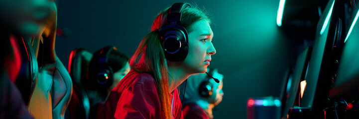 Caucasian teenage girl wearing headset intensely playing video game on computer with diverse...