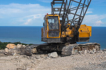 an old crawler crane with a lattice boom, standing on a construction site near a cliff by the sea
