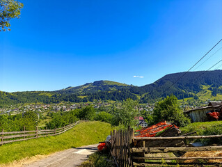 A dirt road in the middle of the herbaceous field next to a wooden fence against the hills background