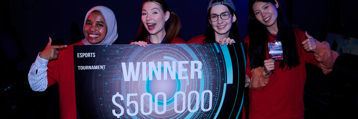 Diverse group of teenage girls gamers celebrating victory holding large esports tournament winner...