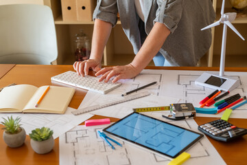 Architect working on sustainable building project using computer and blueprints, with miniature...