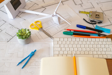 Desk of architect designing a sustainable and ecological building with blueprints, wind turbine...
