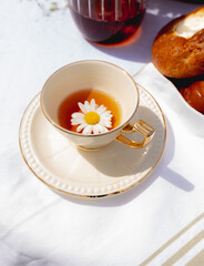 Porcelain cup of chamomile tea with a chamomile flower floating inside on a table with a white tablecloth.