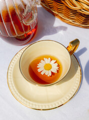 Porcelain cup of chamomile tea with a chamomile flower floating inside on a table with a white tablecloth.