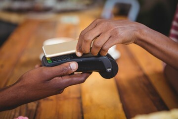 Woman paying bill through smartphone using NFC technology in cafe
