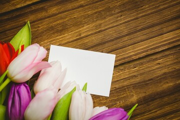 blank white rectangular card is lying atop wooden tabletop in flat-lay, with colorful tulip bouquet