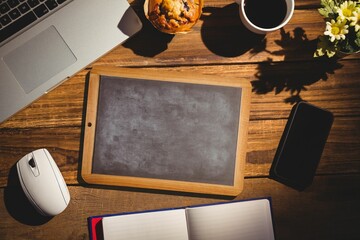 Wooden-framed chalkboard is being shown in flat design workspace with laptop, coffee cup, flowers