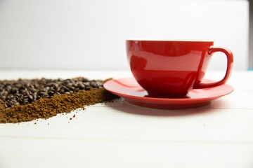 Showing flat-lay red coffee cup resting on wood plank, spilling roasted beans and coffee grounds