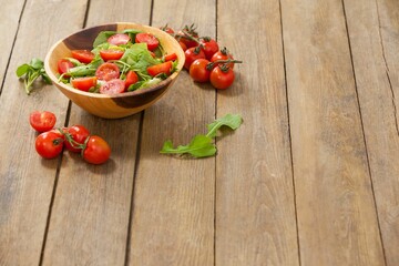 Fresh salad in bowl by cherry tomatoes on table