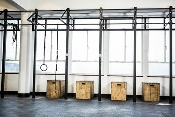 Black metal pull-up rig is spanning gym, featuring gymnastic rings, climbing rope, wooden boxes