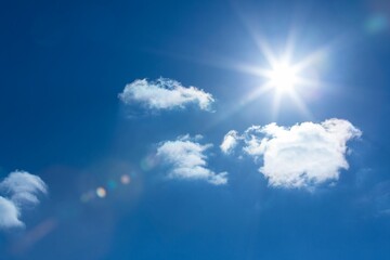 Sun is shining in flat design deep blue sky, with fluffy clouds and vibrant lens flare © vectorfusionart