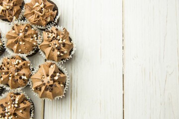 Chocolate cupcakes are being arranged in flat lay style on white painted wooden surface, copy space