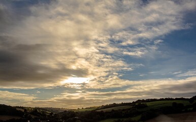 Sunlight is filtering through dramatic sky over rolling green hills and farmland in flat design