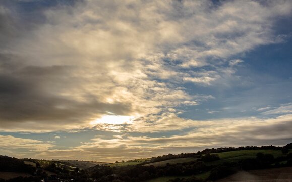 Fototapeta Sunlight is filtering through dramatic sky over rolling green hills and farmland in flat design