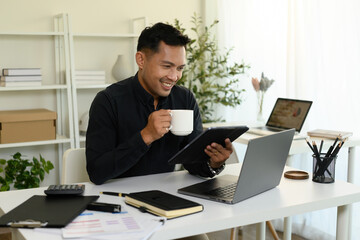 A Mature Asian Businessman Working in Modern Office, Enjoying Coffee While Working Remotely