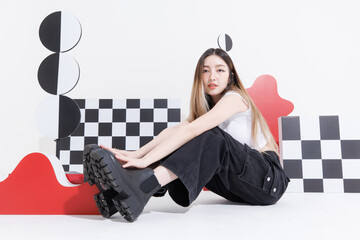Fashionable photo confident woman model asian beautiful female wearing trendy white top shirt black cargo pants casual outfits sitting on floor posing look at camera in studio on colorful background.