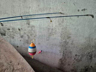 Close-up of fishing rod with colorful float hanging against a weathered concrete wall
