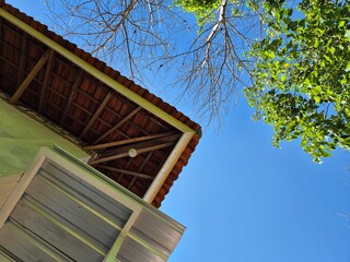 Upward View of House Roof with Tiled Eaves and Tree Branches Against Clear Blue Sky
