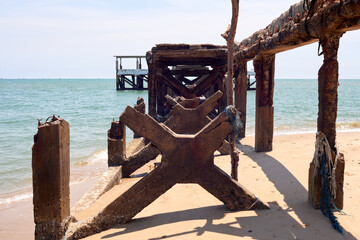 An old, decaying pier on a beach stands against the serene ocean waters.