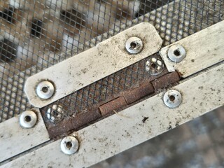 Close-up of Rusty Metal Hinge on Dirty Wire Mesh Door Frame in cricket farm cage
