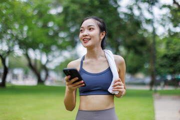 Fototapeta premium Beautiful young asian girl texting and using phone outdoors before workout outdoors in the park. 