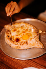 Delicious traditional Adjarian khachapuri served on a metal plate, ready to be enjoyed with a fork