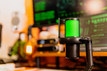 A close-up of a black microphone with green LED lighting, placed in front of multiple computer...