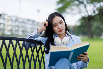 Asian female college student thinking outside with bag and book in a park, Education studying...