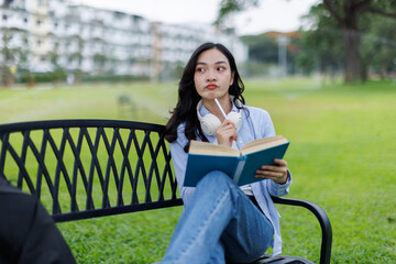 Asian female college student thinking outside with bag and book in a park, Education studying...