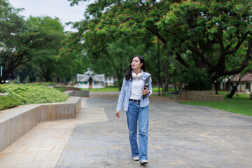 Asian woman student walking in the park chatting by mobile phone in a park, Education studying...