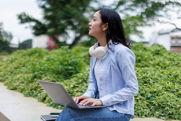 Young asian woman lies outdoors in park reading book using laptop computer Education studying...