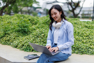 Young asian woman lies outdoors in park reading book using laptop computer Education studying...