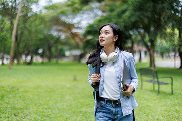 A young asian girl student with notebooks and a folder with headphones in her ears listening to an...