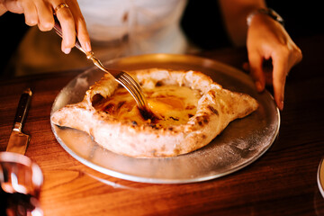 Enjoying Adjarian Khachapuri with a runny egg at a cozy restaurant during dinner time