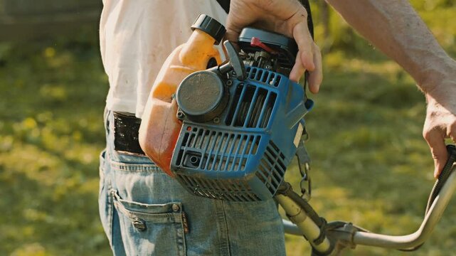 A man pulls the starter handle on a hand-held grass trimmer. Evening gardening