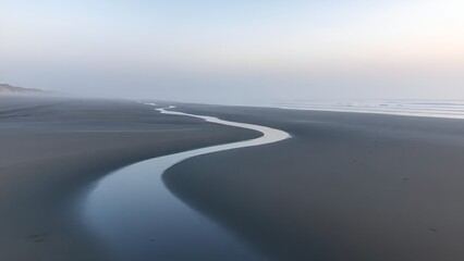 Winding Stream on Serene Foggy Beach at Sunrise with Soft Light
