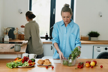 Middle age woman preparing healthy salad in bright kitchen, showcasing active lifestyle, wellness, fitness, and wellbeing for older women.